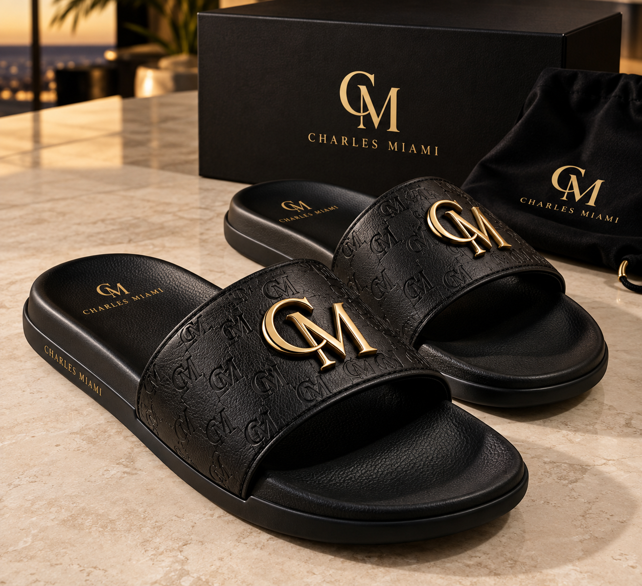 Charles Miami black embossed slides with gold CM emblem beside a black gift box